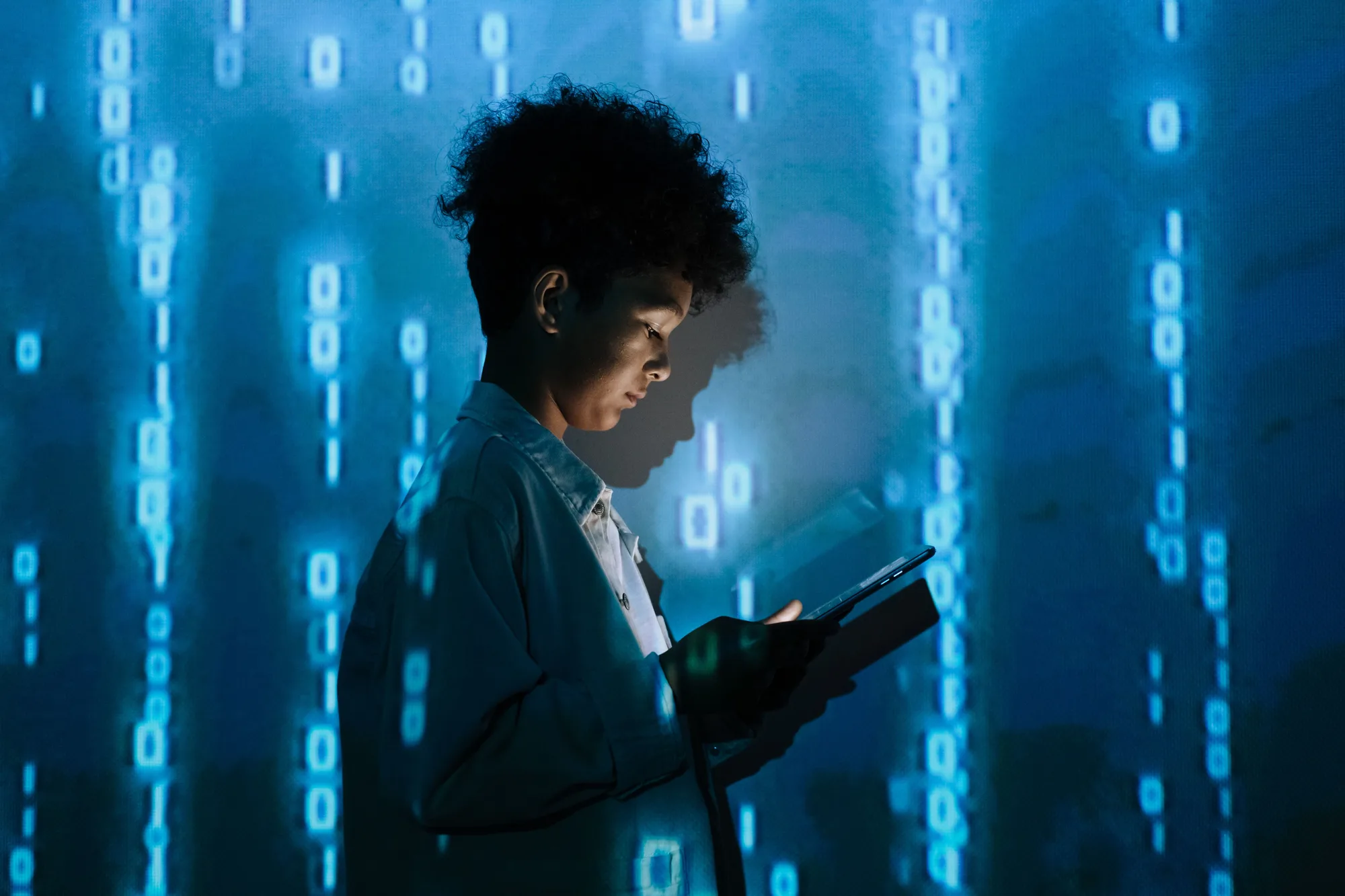 Young woman using a tablet in front of a wall of glowing binary code