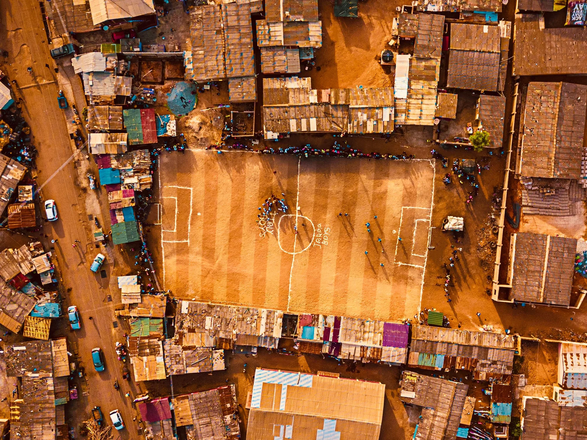 Aerial view of a dirt football pitch surrounded by tightly packed homes