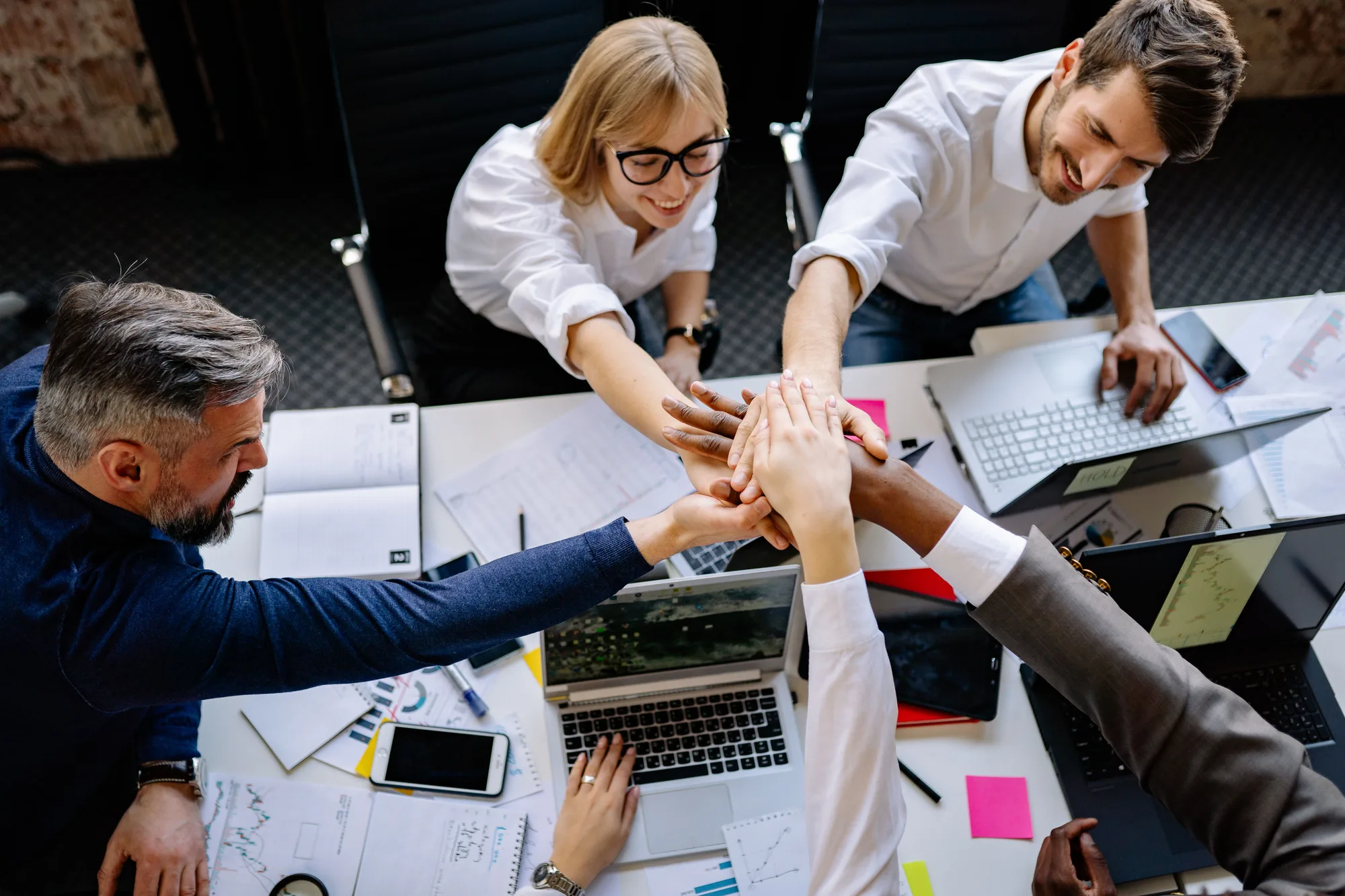 Team stacking their hands together over a desk with laptops