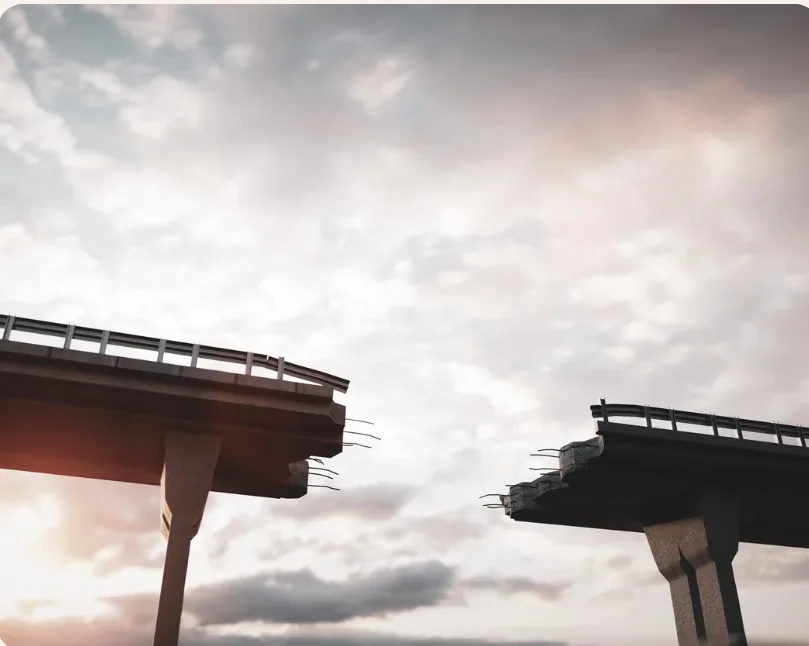 Two halves of a broken bridge reaching toward each other against a cloudy sky